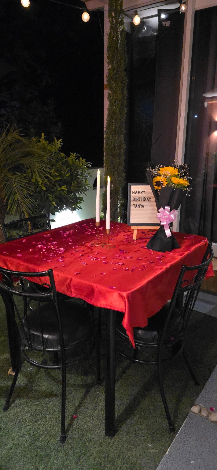 Birthday table décor in the rooftop garden with red linen, flowers, rose petals and candles